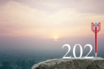 Red pencil in the shape of a dart arrow with 2021 white text on rock mountain over aerial view of cityscape at sunset, vintage style, Business strategy happy new year 2021 cover concept