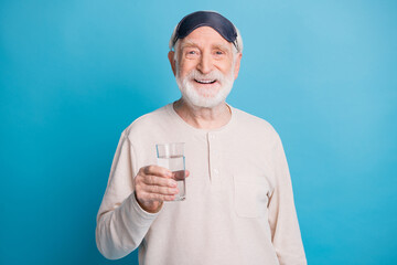 Canvas Print - Photo portrait of elderly man in eye mask holding glass of water isolated on pastel blue colored background