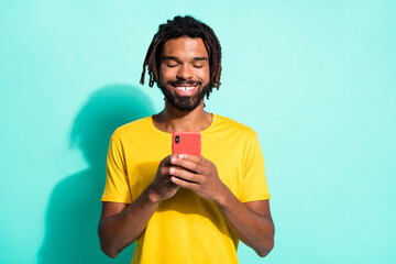 Photo portrait of afro american guy holding phone in two hands isolated on vivid teal colored background