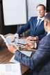 © LIGHTFIELD STUDIOS - African american businessman pointing with pen at document while sitting near thoughtful executive on blurred background.