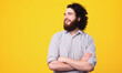 © Vulp - Portrait of cheerful curly and bearded man standing over yellow background with crossed arms.