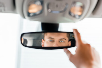 Cropped view of man adjusting rearview mirror in car on blurred foreground.