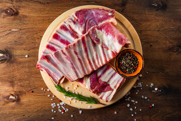  Raw ribs, salt, pepper and rosemary on a round wooden cutting board top view