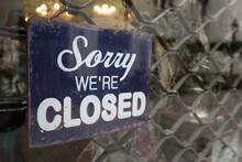 " Sorry We Are Closed " Retro Wooden Sign Is Hanged Behind Glass Of Storefront Of Retail Shop In Front Of Shutter Door.