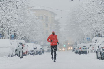 Young man runner under a snowfall in the city