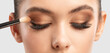 © Dimid - Portrait of a charming brunette woman with healthy clean skin. Makeup artist applies eye shadow.The concept of aesthetic cosmetology and makeup.