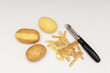 Raw peeled potatoes with a potato peeler on a white table, potato peel.