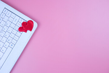 Two red hearts and a keyboard, on a pink background. Online dating. Valentine's Day