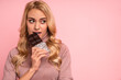 © Roman - Portrait of a happy young woman biting chocolate bar isolated over pink background. Free space for text, logo or advertising