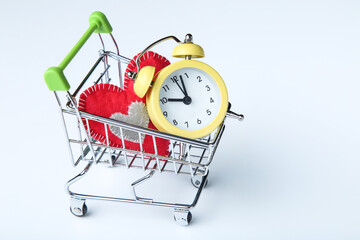 Wall Mural - Alarm clock with red fabric heart and shopping cart on blue background