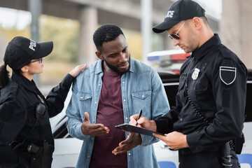 Wall Mural - policewoman calming african american victim talking to policeman with clipboard on blurred background outdoors.