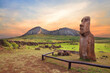 Stone fence and Moai statues at the entrance in the Ahu Tongariki ceremonial center on Easter Island, covered by a colorful sunset sky, against the crater of the Rano Raraku volcano.