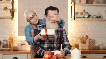 Wall Mural - Happy Valentine's Day. Senior woman giving gift box to husband, cooking lunch at kitchen.