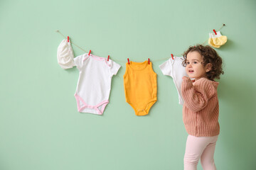 Poster - Cute baby girl near stylish clothes hanging on color wall