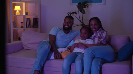 Happy young family gathering together in front of tv watching movie in evening