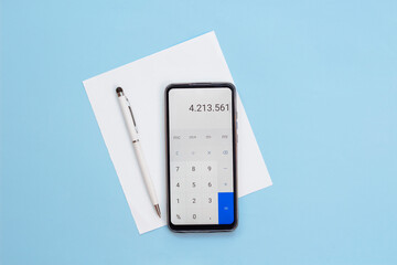 calculator on phone, a pen and a blank white paper on blue background.