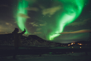 woman with phone against glowing northern lights
