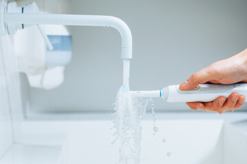 Wall Mural - hand holding a toothbrush under flowing water from faucet in a bathroom