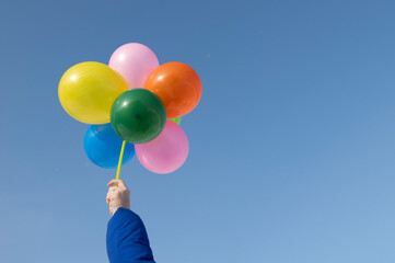 Hand holdind flying helium baloons against bright blue sky. Copy space.