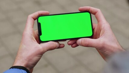 Close up young man holding a smartphone touching phone with horizontal green screen phone on background street. Message business male device digital equipment internet. Slow motion