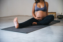 Young pregnant millennial woman sitting on the mat touches her belly after performing prenatal and meditation exercises at a yoga class - Concept of life and maternity