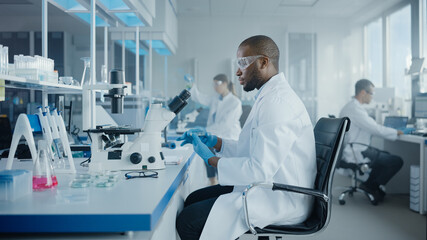 Wall Mural - medical development laboratory: portrait of black male scientist looking under microscope, analyzing