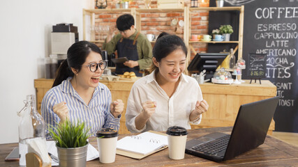 happy college student girls celebrate successful teamwork results in cafe bar. excited two asian woman working on project and pass exam in coffee shop. startup in coffeehouse male owner in counter