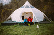 © BublikHaus - Couple of vacation goers campers sit in front of big glamping tent. Happy couple on romantic weekend getaway with pet dog. Fun and luxury camping experience in nature