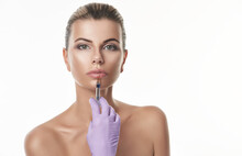 Lips Augmentation Concept. Beautiful Young Woman With Purple Gloves Holding A Syringe Ang Making Injection On Lips.