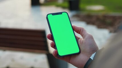 Close up young hands man holding use phone with vertical green screen in park background bench. Internet finger gadget device. Slow motion