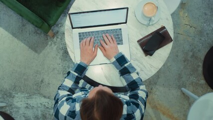 Top view on middle aged adult man sitting at cafe, working on laptop, remotely from outside the office. Zoom out shot of freelancer working. Work from home or from coworking modern space