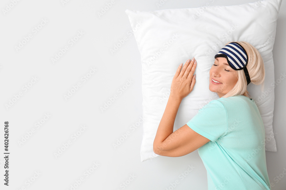 Mature woman in sleep mask on light background