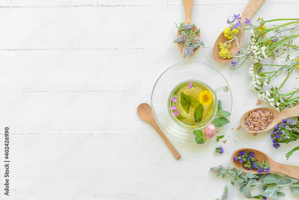 Flowers, spoons and cup with floral tea on light background