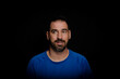 © Andres - Bearded man dressed in blue t-shirt posing against black background
