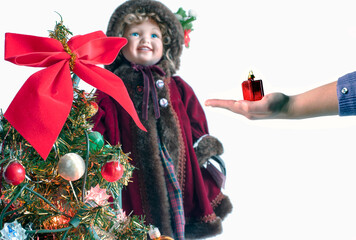 Girls decorating the Christmas tree.  A girl’s hand holding a bauble near a decorated Christmas tree with a smiling baby doll in the background isolated on white.