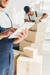© LIGHTFIELD STUDIOS - cropped view of worker in uniform holding digital tablet near indian coworker packing box on blurred background