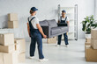 © LIGHTFIELD STUDIOS - full length of happy young multiethnic movers in uniform carrying couch in apartment