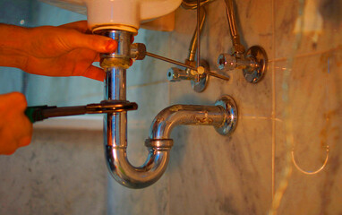 A close up of a hand holding a plumbing spanner screwing a fitting on wash basin waste pipe. 