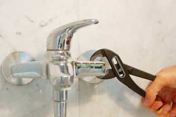 A close up of a hand holding a plumbing spanner screwing a fitting on wash basin waste pipe. 