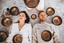 Group Therapy With Tibetan Singing Bowls For A Girl And A Boy Lying On The Ground In The Middle Of The Desert Surrounded By Copper Bowls, Meditation And Relaxation