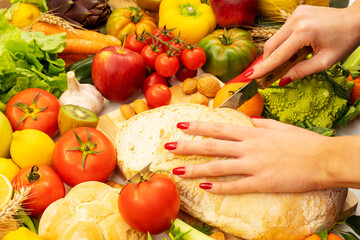 Wall Mural - A close up on the hands of a cook cutting a piece of bread on a table with various types of vegetables