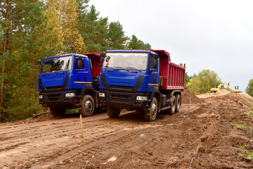 Wall Mural - Dump trucks work on road construction in a forest zone. Tipper truck transport sand for roadworks project