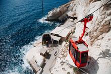 Rosh HaNikra. Red Cable Car  Descends On The Background Of Sea,  Stones, Rocks And Mountains