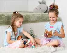 Peaceful Calm Kid Girls Sisters In Home Dresses Spend Time Together Talking And Playing With Their Dolls At Home. Happy Childhood, Cheerful Lifestyle, Games, Comfortable Pastime, Hobby Concept
