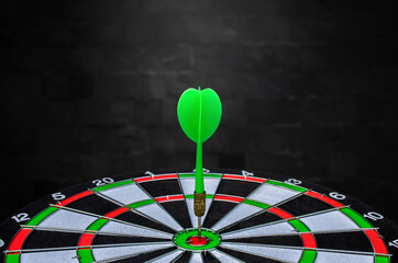 Planning new business target and goals, Green dart arrow hitting in the target center of dartboard with black wall background. achieve and victory concept