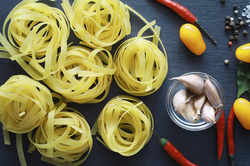 Wall Mural - Pasta on the table with spices and vegetables. Noodles with vegetables for cooking on a black stone background.