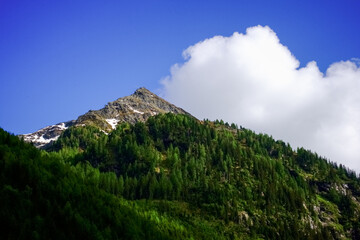 rocky mountain with trees and some snow with blue sky