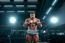 Bodybuilder Athlete Man Pumping Up Muscles In The Gym. Brutal Strong Muscular Guy On Fitness Workout. Bodybuilding Concept.