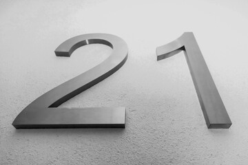 Number twenty one on texture light wall, symbolizing year 2021. Chrome numerals 21 on textured surface white color gradient background. Monochrome background with numbers two and one. Copy space