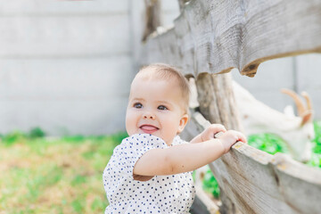 blond beautiful baby smiling showing tongue near the corral for goats on the ranch